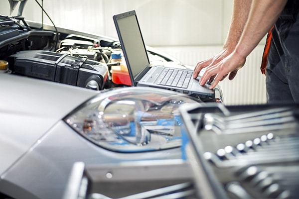 Person with laptop computer running Mechanical diagnostics at the open hood of a car