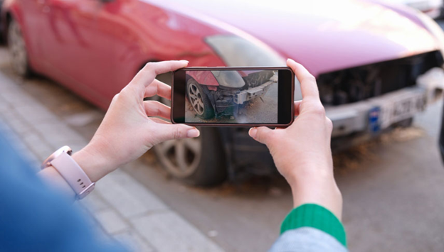 woman taking picture with cell of her damaged car